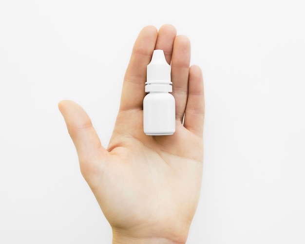 Hand holding white bottle with eye drops on white background