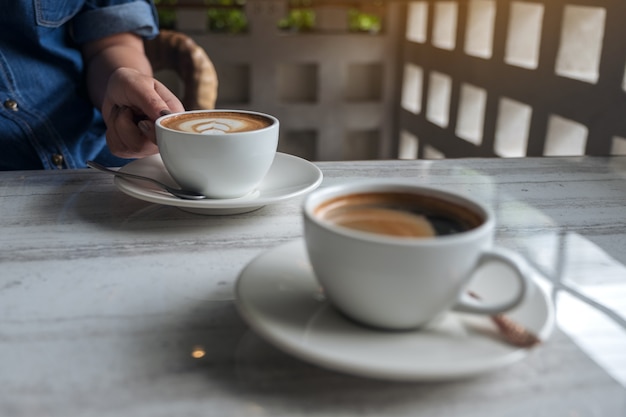 熱いラテコーヒーの白いカップを持っている手