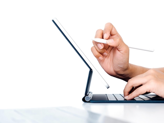 Hand holding white electronic pen or pencil writing or drawing on digital tablet screen while typing on keyboard computer isolated on white background with space side view Work with technology