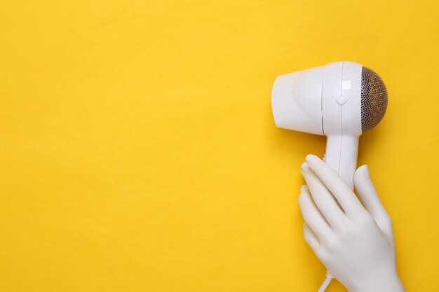 Photo hand holding white hair dryer on yellow background beauty concept hair care hair style top view flat lay copy space