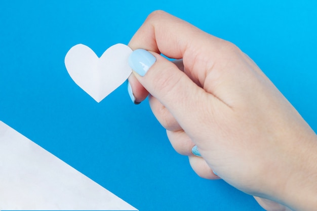 Hand holding a white heart on a white and blue background