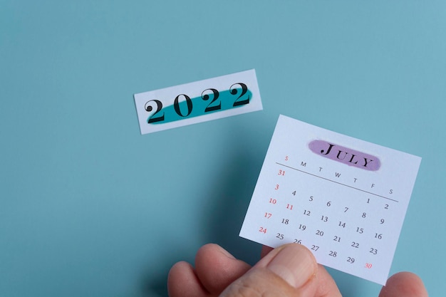 Foto mano che tiene un calendario bianco di luglio con sfondo verde dell'anno 2022 del blocco note. concetto di capodanno