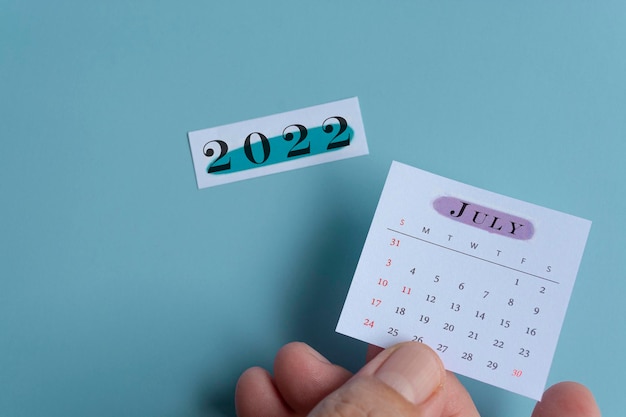 Hand holding a white july calendar with green background of
notepad year 2022. new year concept