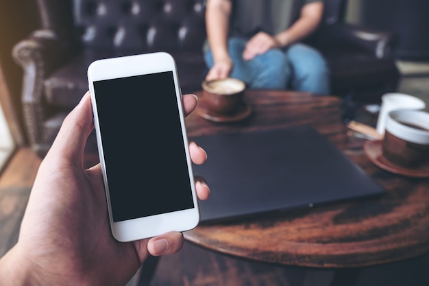 hand holding white mobile phone with blank black screen in cafe