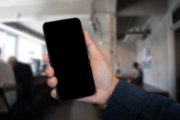 Рука держит белый мобильный телефон с пустым белым экраном в кафе
