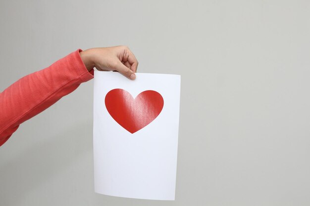 A hand holding a white paper with red heart printed