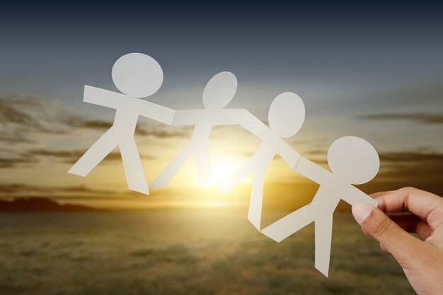 Photo hand holding white people paper holding hands with sunset scene background. world population day concept