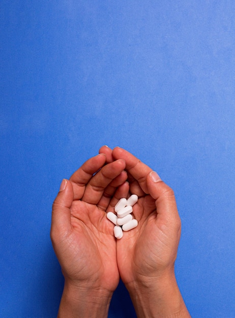 Hand holding white pills on blue background. Copy space.