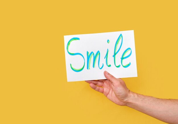 Hand holding a white poster board with the text smile isolated on a yellow background