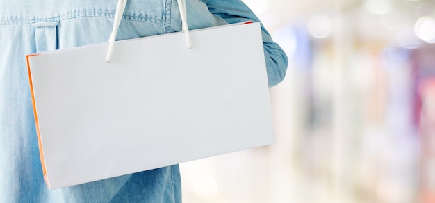 Photo hand holding white shopping bag on blur store background
