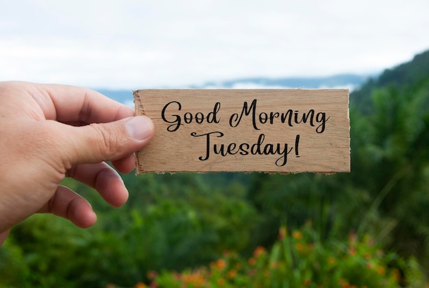 Hand holding wooden banner with Good Morning Tuesday text With beautiful nature background Morning wishes concept