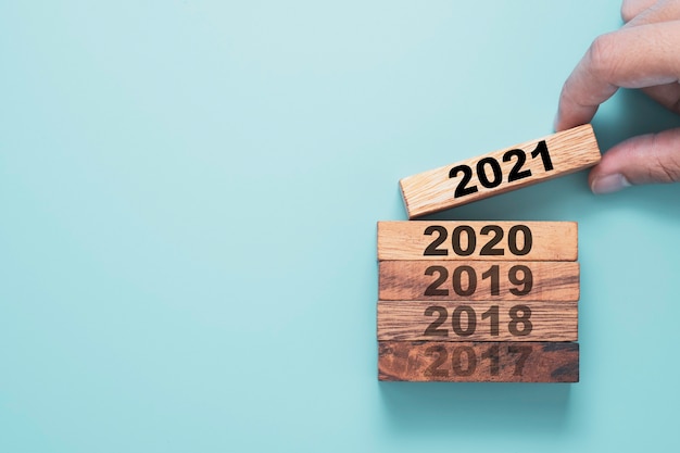 Рука держит деревянный кубик, который печатает экран 2021 года и кладет поверх 2020 года с синим фоном.