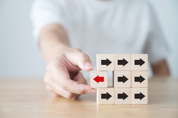 Hand holding wooden block with red arrow facing the opposite direction black arrows, Unique, Think different, Individual and standing out from the crowd concept