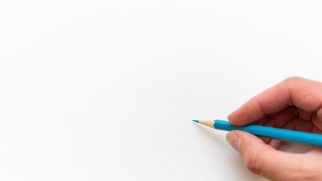 Foto mano che tiene una matita semplice tagliente blu in legno per disegnare o fare schizzi su sfondo bianco del foglio bianco, primo piano, copia spazio. torna al concetto di scuola.