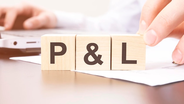 Hand holding wooden cube with P and L text on table background financial marketing and business concepts