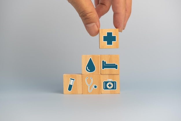 Hand holding wooden cubes block with insurance health car medical symbol on background and copy space