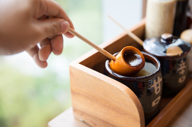 Hand holding wooden dipper with tonkatsu sauce in jar