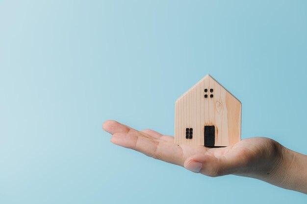 Photo hand holding a wooden house model on blue background