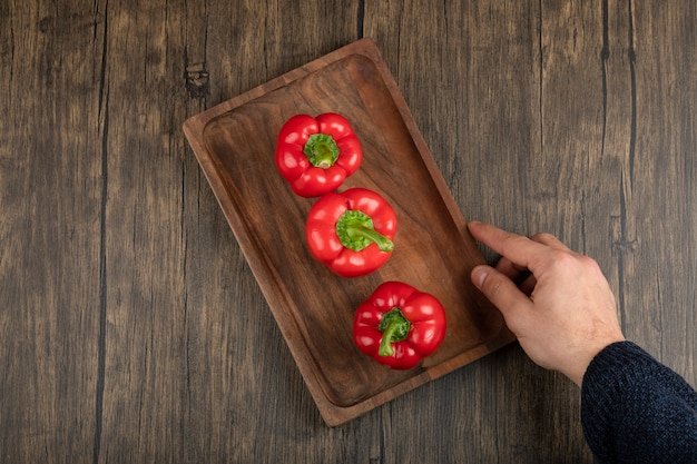 Рука держит деревянную тарелку свежего красного болгарского перца на деревянной поверхности