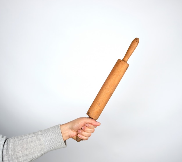 Hand holding a wooden rolling pin on a gray background