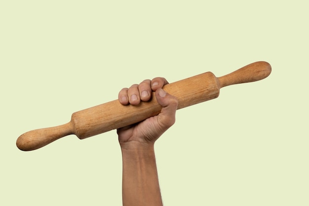 Hand holding a wooden rolling pin isolated on light green background