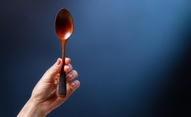 Foto mano che tiene il cucchiaio di legno per la zuppa artigianale di posate da cucina fatte a mano su sfondo blu