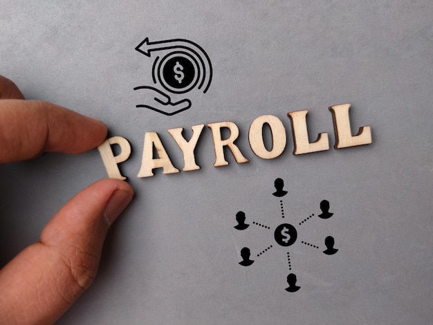 회색 배경에 텍스트 PAYROLL이 있는 나무 단어와 아이콘을 들고 있는 손