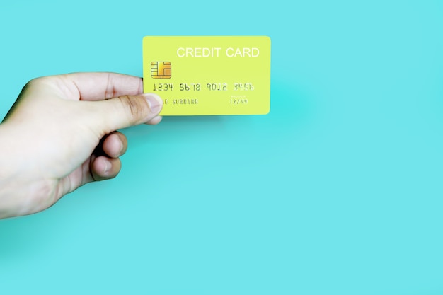 Hand holding a yellow credit card on a blue background, credit card can be used to pay for goods or services, credit card concept, holding credit card clipping path.