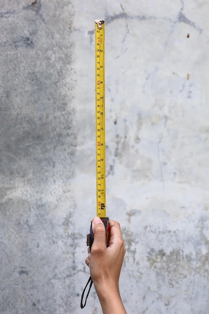 Hand holding a yellow measuring tape over grey concrete background