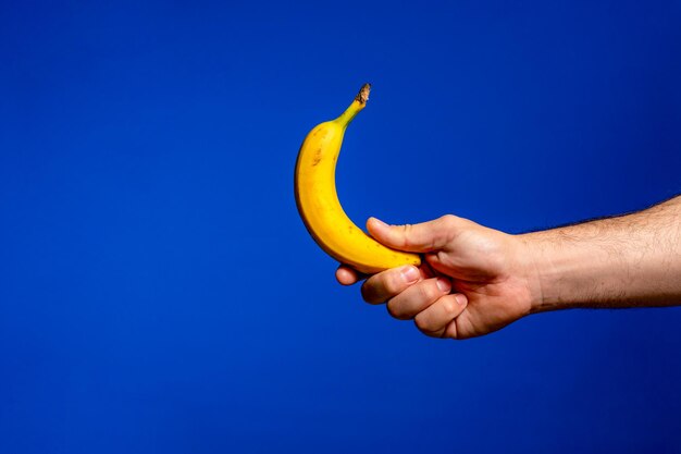 Hand holds banana isolated on blue background alpha person