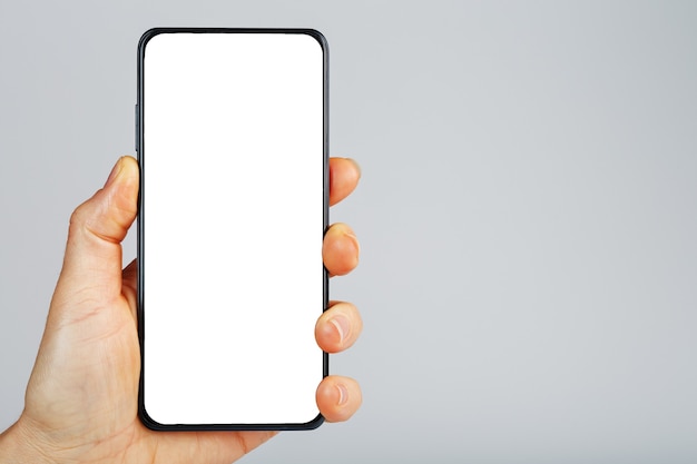 Hand holds black smartphone with blank white screen and modern frameless design isolated on gray surface
