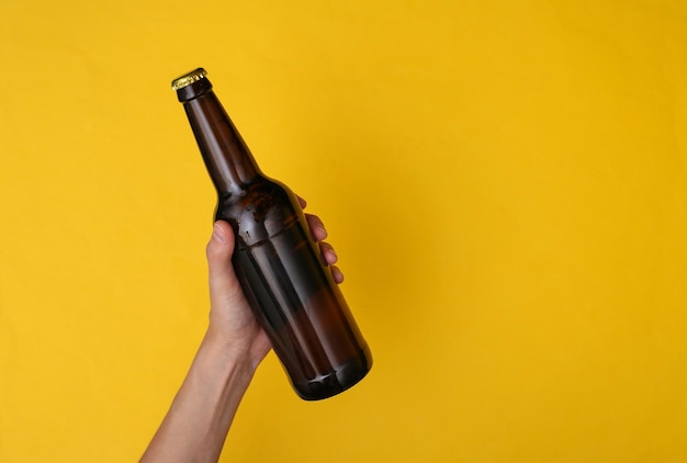 Hand holds a bottle of beer on yellow background