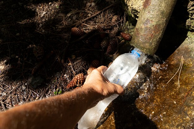 Foto la mano tiene una bottiglia e la riempie di acqua da un ruscello naturale