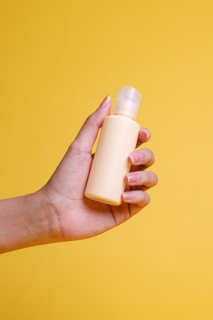 Hand holds bottle for mock up on yellow background Space for design concept of skin care