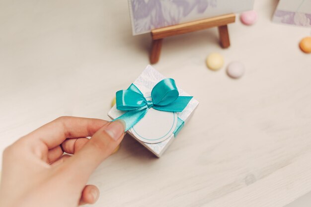 Hand holds bow of blue gift on wooden table