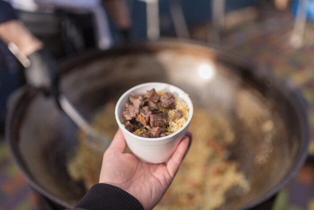 Hand holds bowl with meat and rice.