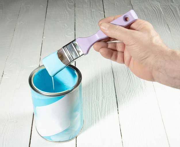 The hand holds a brush with a light blue paint flowing from it in a jar