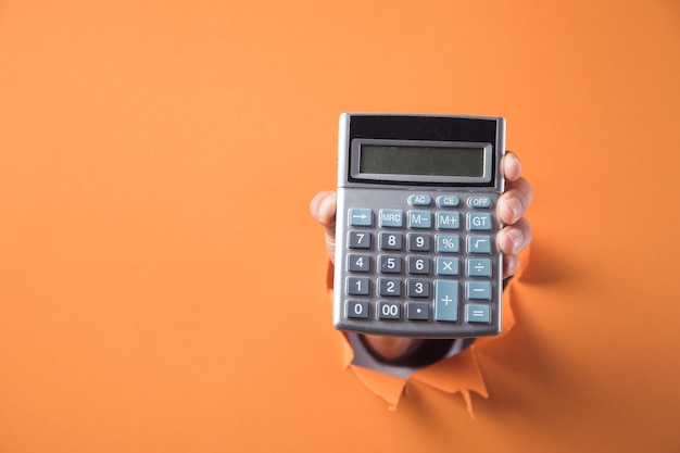 Hand holds calculator on orange background