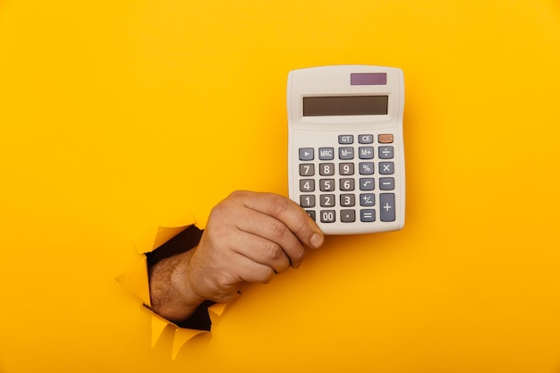 Hand holds calculator through a paper hole in yellow background