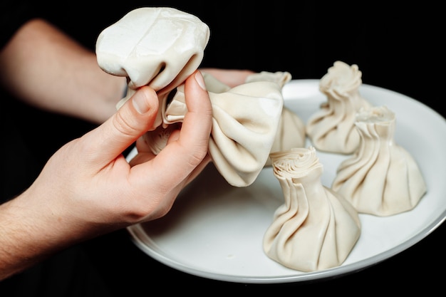 The hand holds the chikali by the tail. Khinkali in a Georgian restaurant in hand. Georgian cuisine.