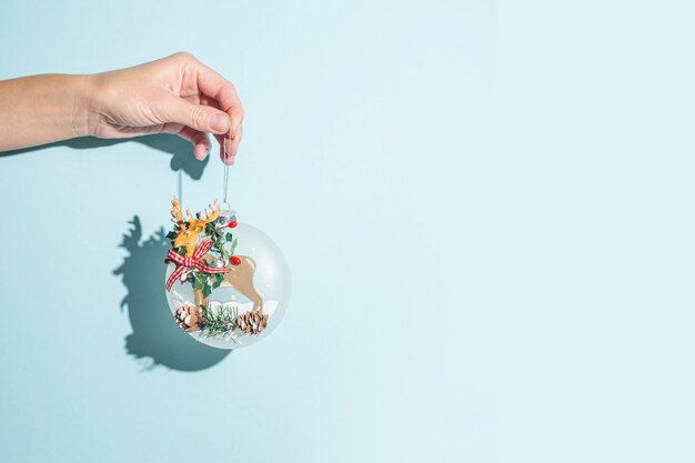 Hand holds a Christmas tree decoration on a blue background. Hard light.