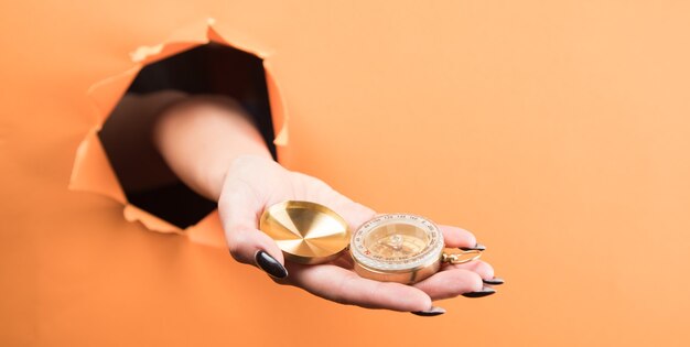 Hand holds compass on orange background