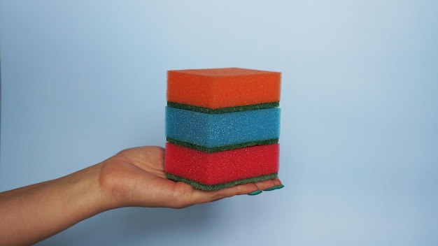 Hand holds different sponges on a blue background.