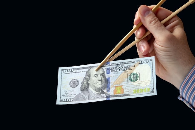 Hand holds dollars with bamboo chopsticks on a dark background financial industry in food cash spending concept