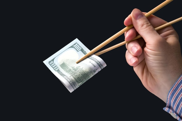 Hand holds dollars with bamboo chopsticks on a dark background financial industry in food cash spending concept