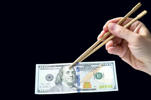 Hand holds dollars with bamboo chopsticks on a dark background financial industry in food cash spending concept