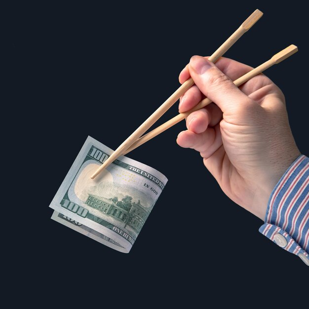 Hand holds dollars with bamboo chopsticks on a dark background financial industry in food cash spending concept