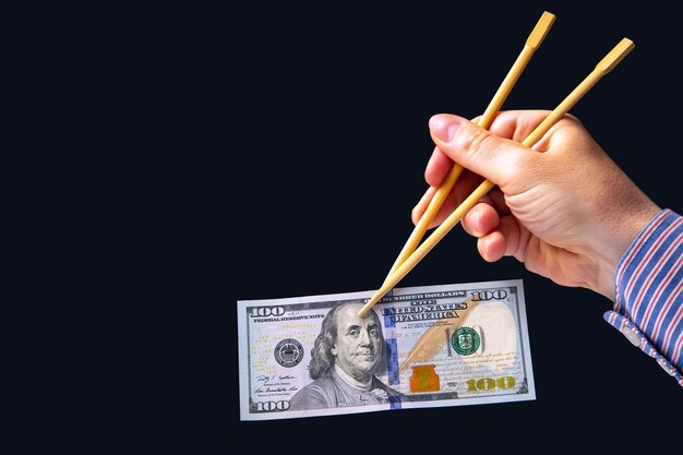 Hand holds dollars with bamboo chopsticks on a dark background financial industry in food cash spending concept