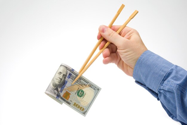 手は、食品の現金支出の概念で白い背景の金融業界に竹の箸でドルを保持します