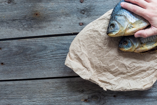 Hand holds Dried Volga bream vobla in a crumpled kraft paper roll, delicious beer snack